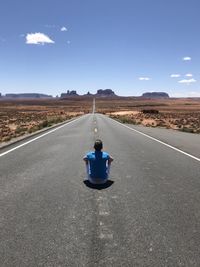 Rear view of man sitting on road against landscape