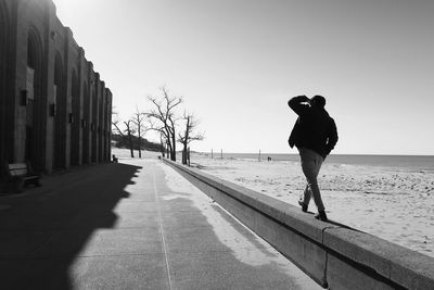 Rear view of man walking on retaining wall at beach against sky