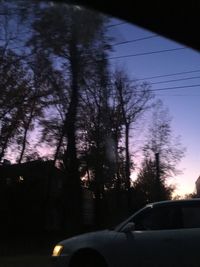 Silhouette trees against sky seen through car windshield