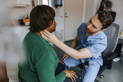 Male medical professional checking female patient's neck while sitting on chair in examination room