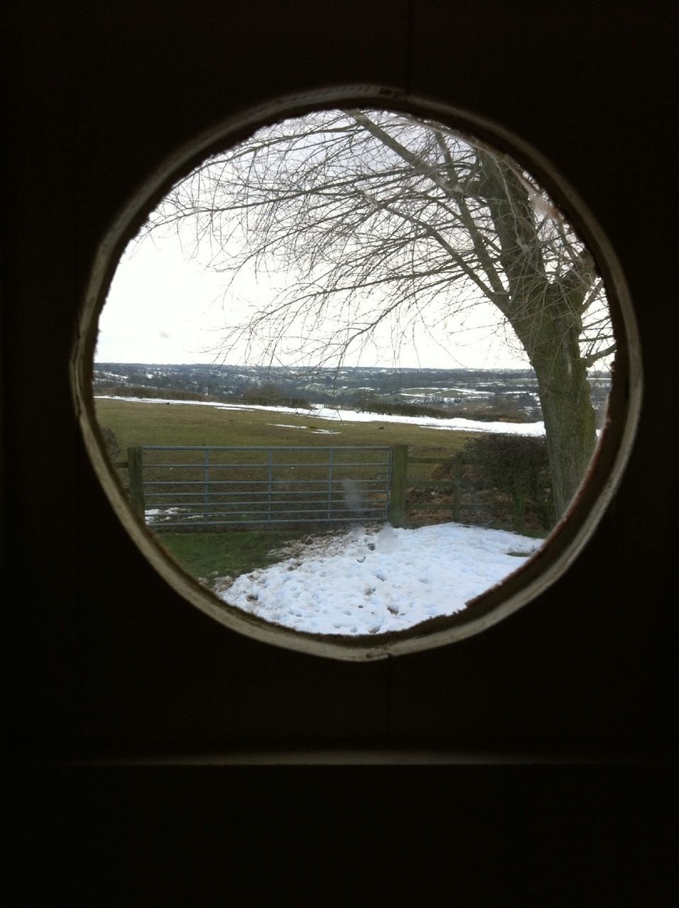 circle, window, indoors, winter, tree, transparent, snow, landscape, season, geometric shape, cold temperature, reflection, sky, glass - material, weather, water, nature, bare tree, tranquility, round