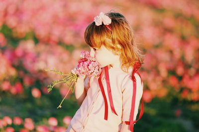 Cute girl smelling pink flowers while standing on land