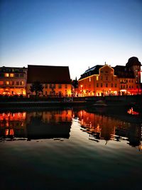 Illuminated buildings by lake against sky at dusk