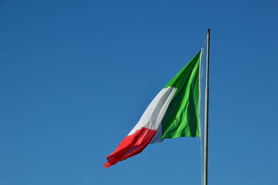 Low angle view of flag waving against clear blue sky