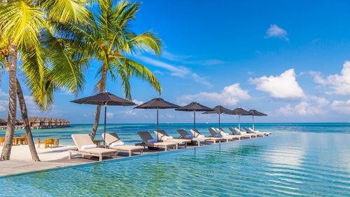 Luxury resort poolside with beach view, horizon and blue sunny sky. luxury vacation chairs umbrellas