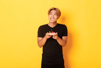 Smiling young man standing against yellow background