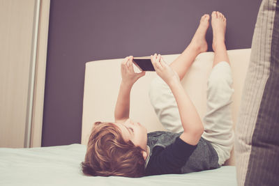 Boy with mobile phone lying on bed