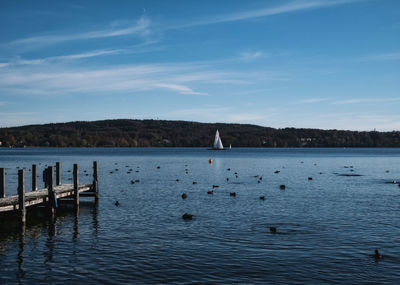 Scenic view of lake with pier and sailing boat against blue sky 