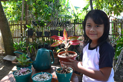 Portrait of smiling girl with potted plants on table sitting in yard