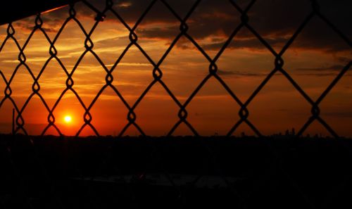 Close-up of silhouette chainlink fence against sunset sky