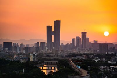 Modern buildings in city against sky during sunset