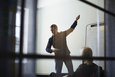 Businesswoman looking at male professional giving presentation against wall in board room seen from glass at creative of