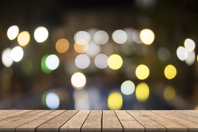 Close-up of wooden table against illuminated lights