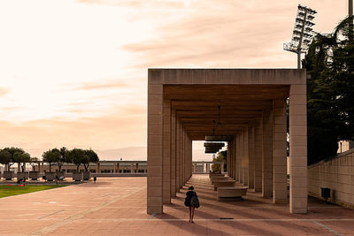 Rear view of woman walking on building against cloudy sky