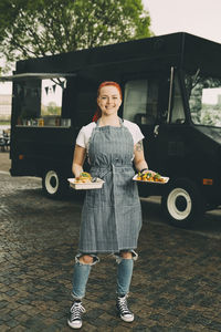 Portrait of smiling owner holding indian food plate on street against commercial land vehicle