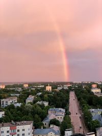 Rainbow over buildings in city against sky at sunset