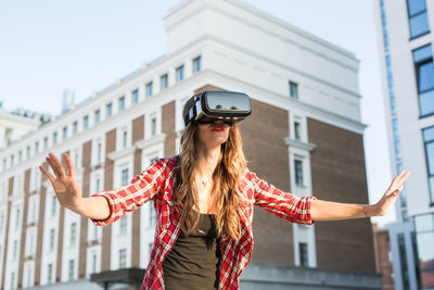 Young woman using mobile phone while standing against buildings