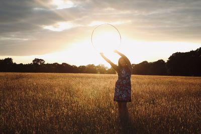 Woman standing on field against sky during sunset