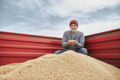 Portrait of man sitting against red wall against sky