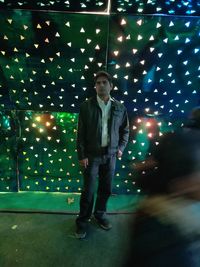 Full length portrait of young man standing against illuminated lights