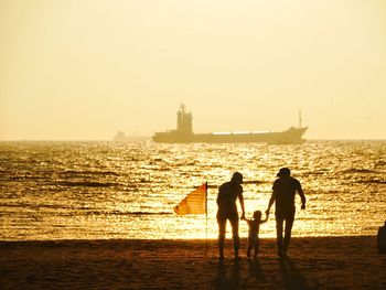 Silhouette people on beach against sky during sunset