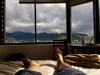 Low section of man relaxing on bed against window