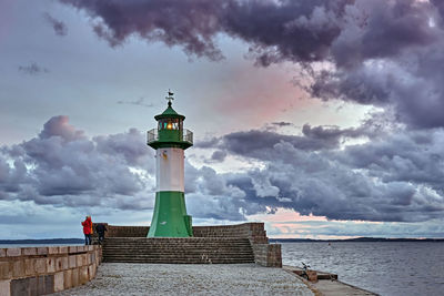 Lighthouse amidst sea and buildings against sky