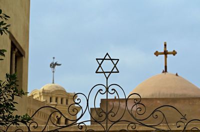 Low angle view of cross amidst buildings against sky