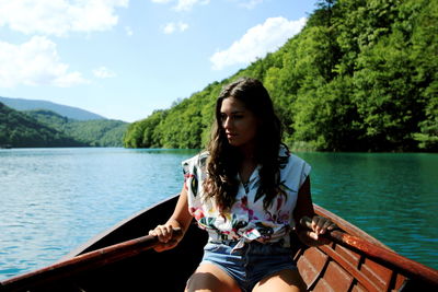 Beautiful young woman sitting on boat sailing in lake against sky
