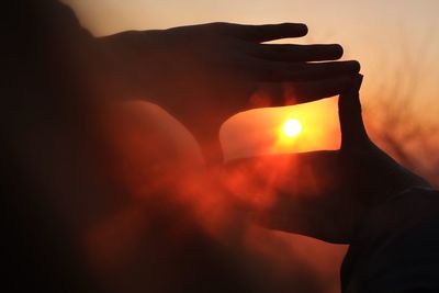 Close-up of hands framing the sun at sunset