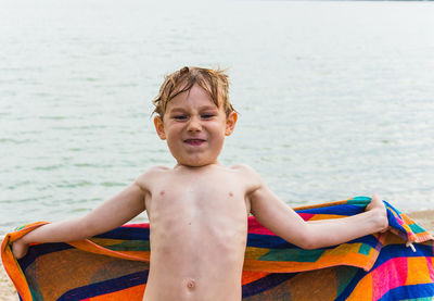Portrait of shirtless boy holding towel against sea