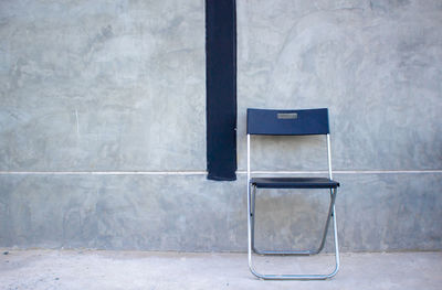 Empty chair by window on wall of building