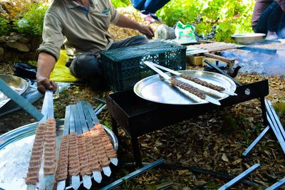 Low section of man sitting by barbecue on field