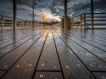 Wet pier against sky during sunset