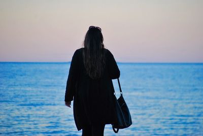 Rear view of woman standing by sea against clear sky