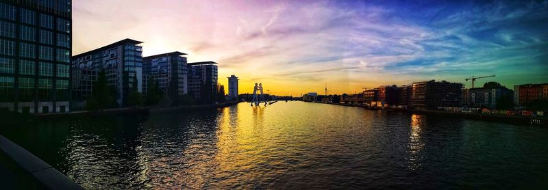 Scenic view of river by buildings against sky during sunset