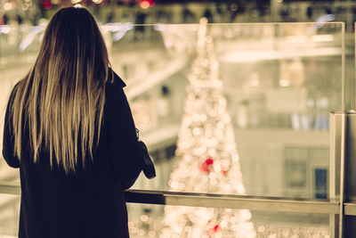 Rear view of woman standing by christmas tree