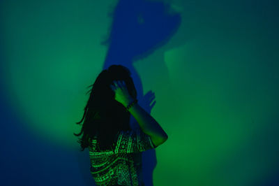 Woman standing against illuminated green wall with shadow