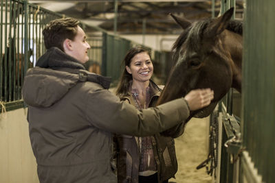 Happy young couple stroking horse in stable