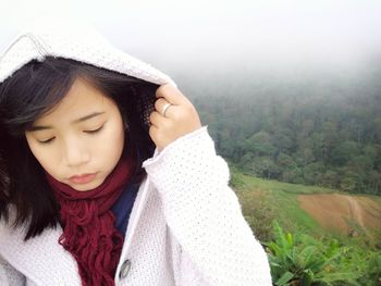 Thoughtful young woman wearing hooded sweater against green landscape