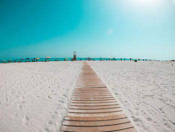 Boardwalk on beach against clear blue sky