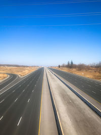 Road passing through landscape against clear blue sky