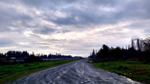 Road passing through field against cloudy sky