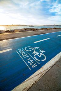 Text on road by sea against sky