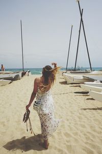 Full length rear view of woman walking on sand amidst boats at beach