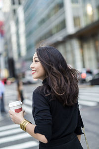 Usa, new york city, manhattan, smiling young woman with coffee to go crossing the street