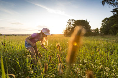 Cute girl standing amidst plants against sky during sunset