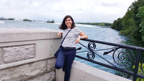 Portrait of young woman standing on retaining wall against sea