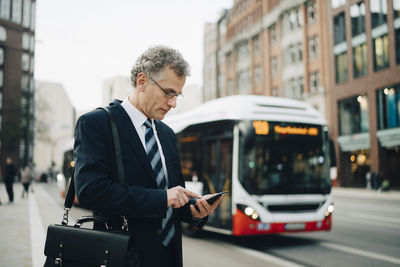 Mature businessman using smart phone while standing in city