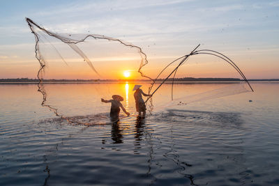 Silhouette man fishing in sea against sky during sunset